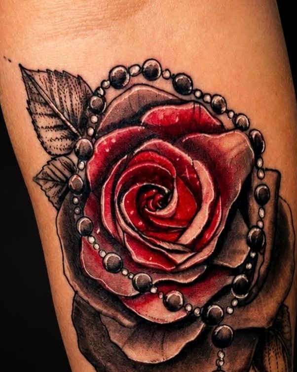 Color realism rose wrapped in a rosary, on a forearm.