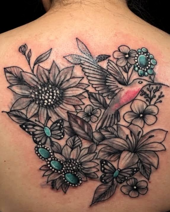 Black-and-grey back piece — a hummingbird among sunflowers and lilies, picked out with turquoise stones.