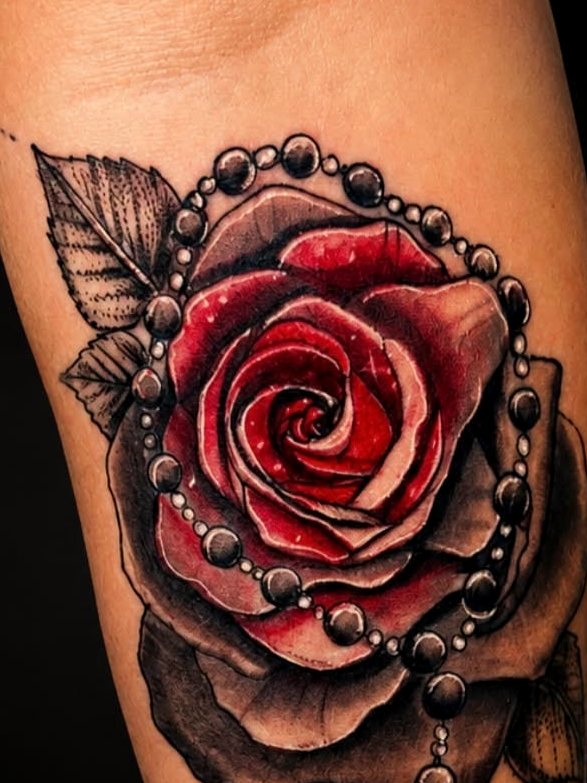 Color realism rose wrapped in a rosary, on a forearm.