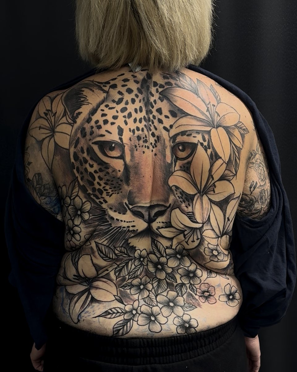 Black-and-grey leopard back piece framed by florals, spanning a full back.