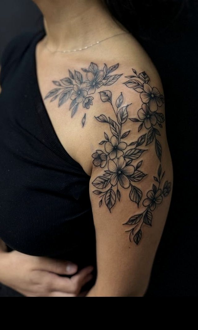 Black-and-grey fineline floral tattoo cascading down a shoulder and upper arm.