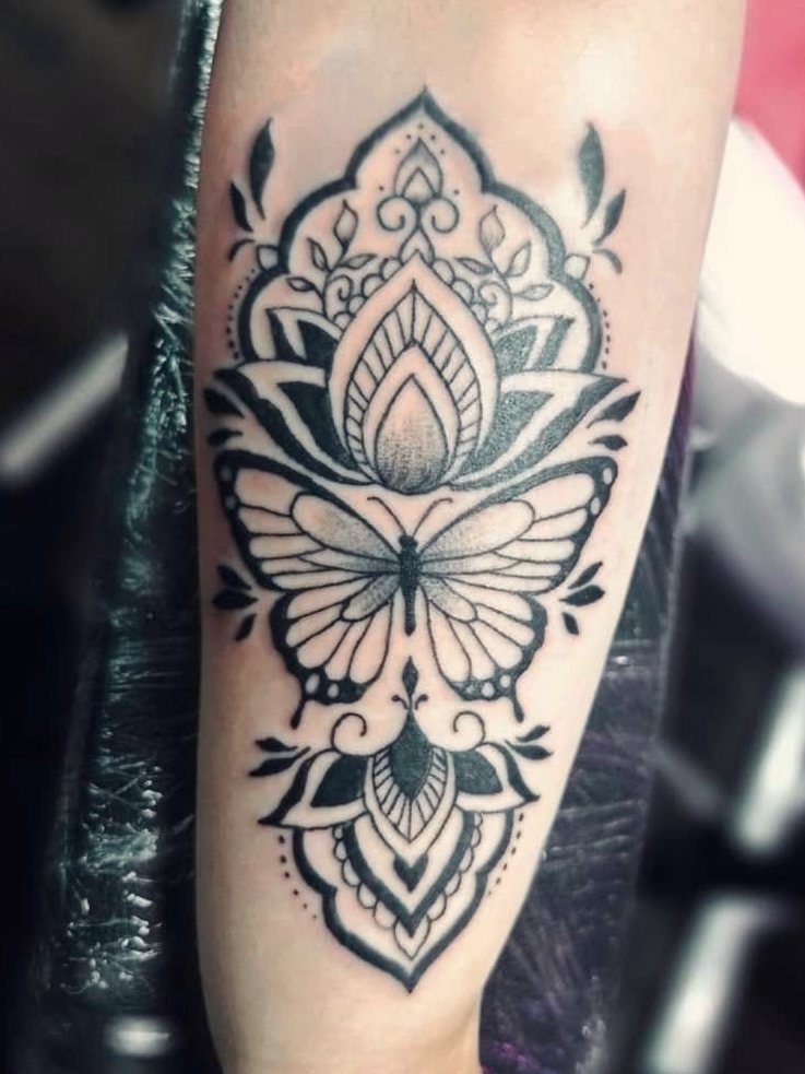 Ornamental dotwork mandala with a lotus and butterfly on a forearm.