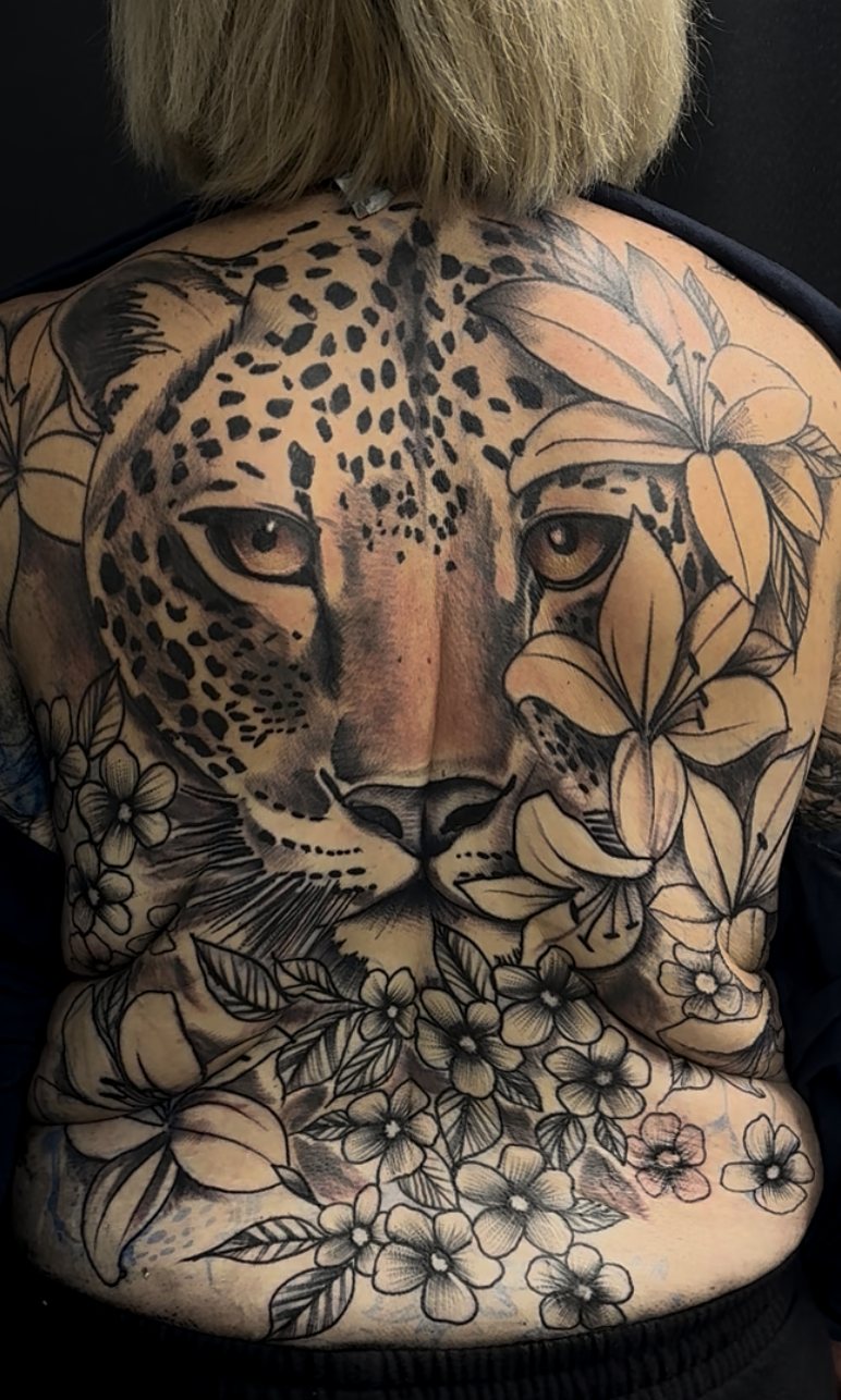 Black-and-grey leopard back piece framed by florals, spanning a full back.
