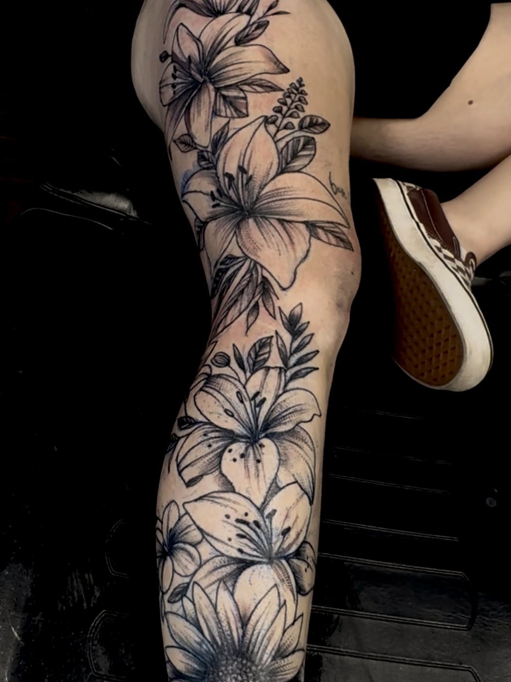 Black-and-grey floral leg piece — lilies and a sunflower down the leg.
